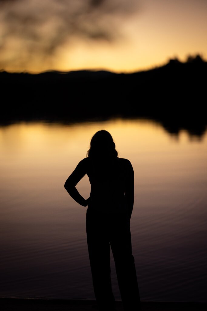 An image of a young Woman's silhouette as outlined with a lake lit by the rising sun.