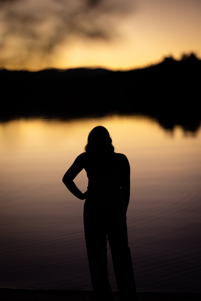 An image of a young Woman's silhouette as outlined with a lake lit by the rising sun.