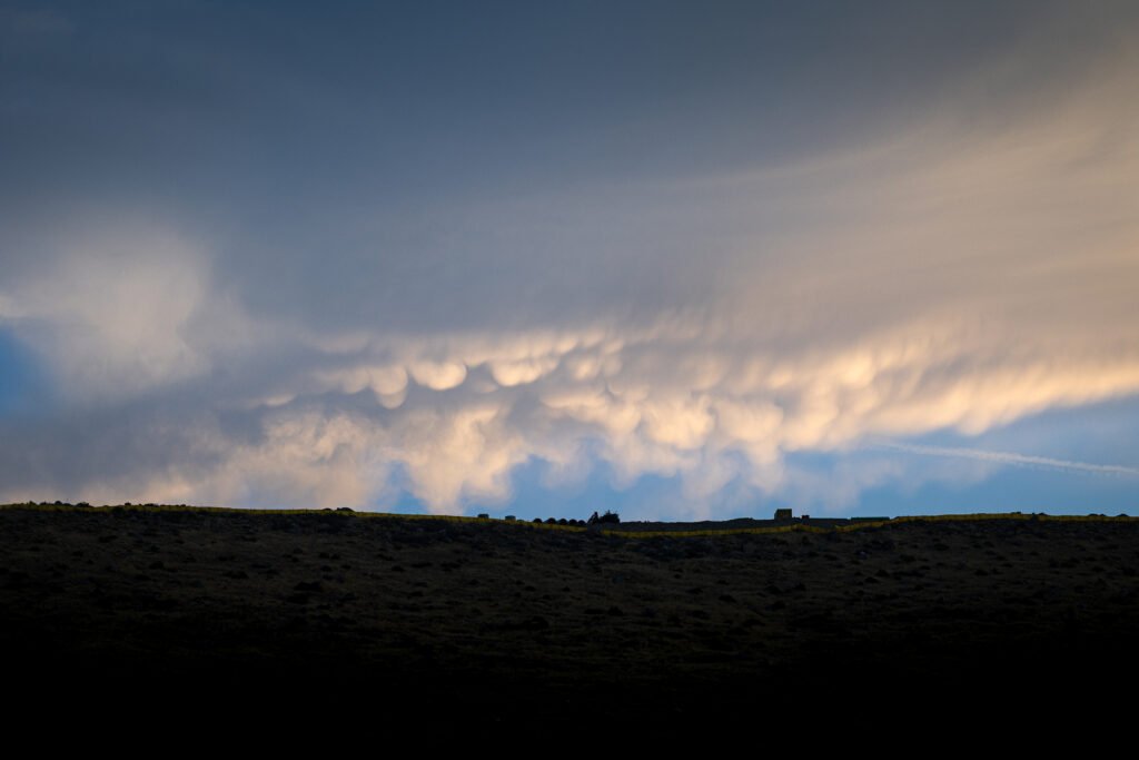 A cloud with a slightly mammatus appearance is lit by the morning sun.
